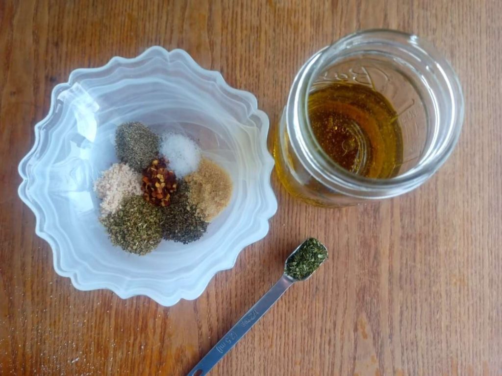 Spices in a bowl next to jar and a tsp on a table