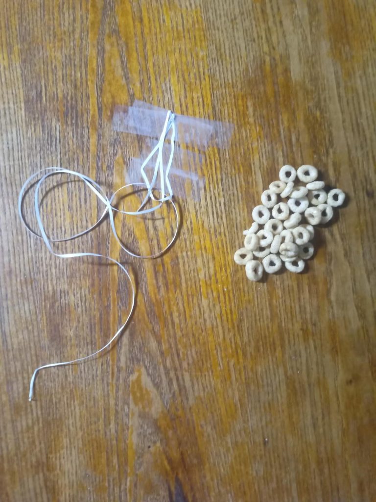 Peice of string taped to a table with a pile of cheerios next to it for a cheerio necklace